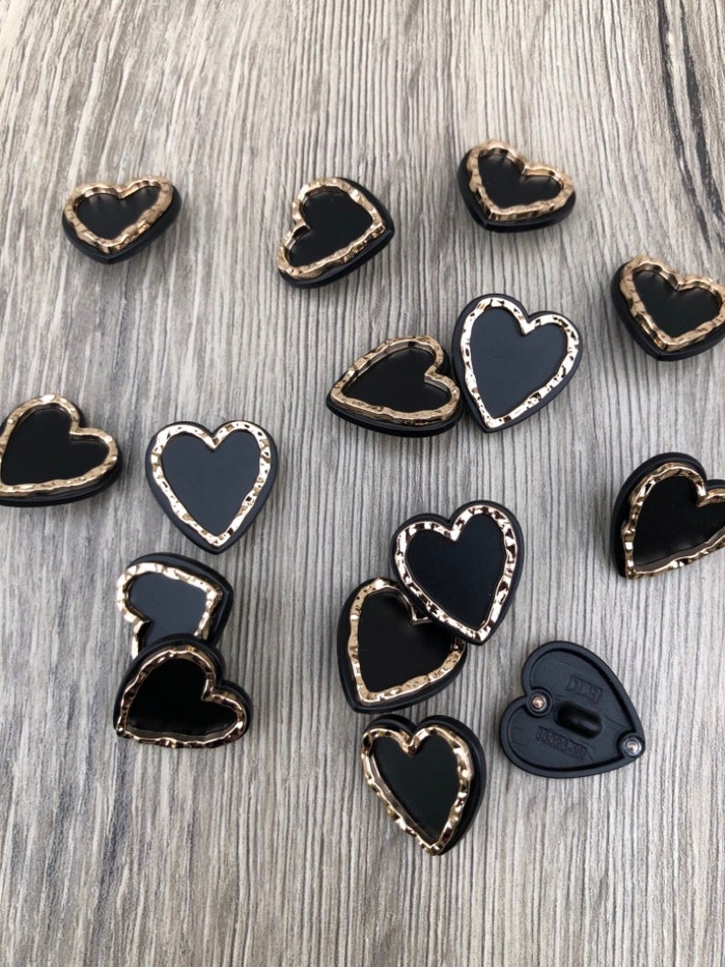 May include: A collection of black heart-shaped buttons with gold-colored edges. The buttons have a textured, slightly raised design around the edges.
