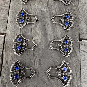 May include: Eight silver-toned metal embellishments with a decorative floral design and three blue rhinestones each.