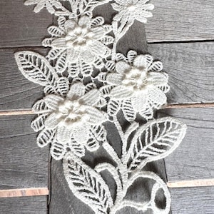 May include: White lace applique with a floral design. The applique features delicate flowers and leaves, and is perfect for adding a touch of elegance to any project.