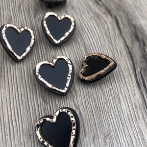 May include: Five black heart-shaped buttons with gold-colored edges. The buttons have a slightly textured surface.