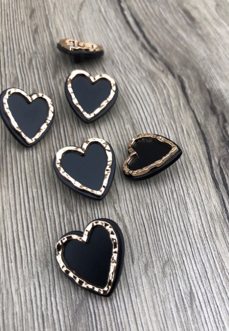 May include: Five black heart-shaped buttons with gold-colored edges. The buttons have a slightly textured surface.