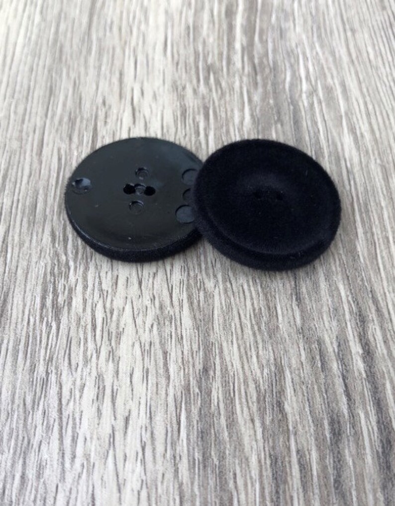 May include: Two black buttons, one with a smooth surface and the other with a textured surface and multiple holes.