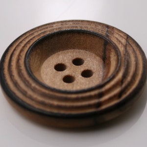 May include: A brown wooden button with four holes and a concentric circle design.