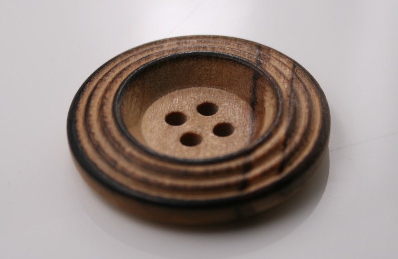 May include: A brown wooden button with four holes and a concentric circle design.