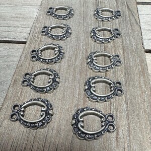 May include: Ten silver-toned metal decorative embellishments with a scalloped oval design. Each embellishment has two loops on the top.