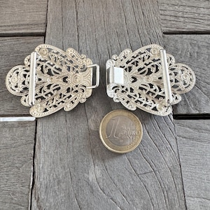 May include: Two silver filigree belt buckles with a decorative floral design. The buckles are about the size of a Euro coin.