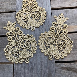 Puede incluir: Tres aplicaciones de encaje dorado en forma de corazón con intrincados diseños florales.