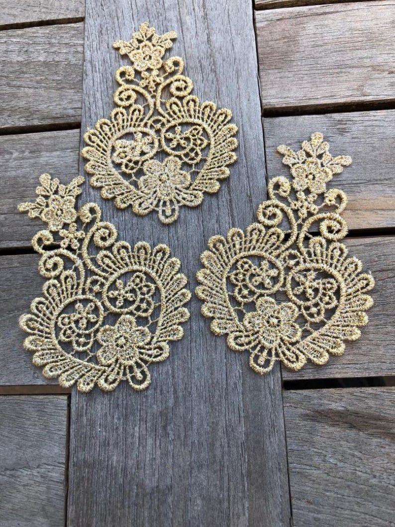 May include: Three gold lace appliques in the shape of a heart with intricate floral designs.