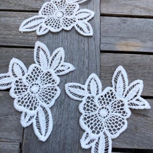 Op de afbeelding: Drie witte kantbloem applicaties met ingewikkelde ontwerpen. De applicaties zijn perfect om een ​​toets van elegantie toe te voegen aan elk project.