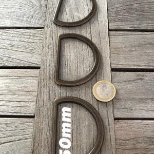 May include: Three D-ring buckles in different sizes, made of metal with a dark bronze finish. The smallest buckle is labelled "50mm".