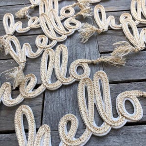 May include: Multiple gold and white "hello" word cutouts with fringe accents. The cutouts are made of a woven material and are arranged on a wooden surface.