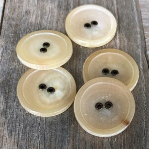 May include: Five round, cream-colored buttons with two brass buttonholes each.