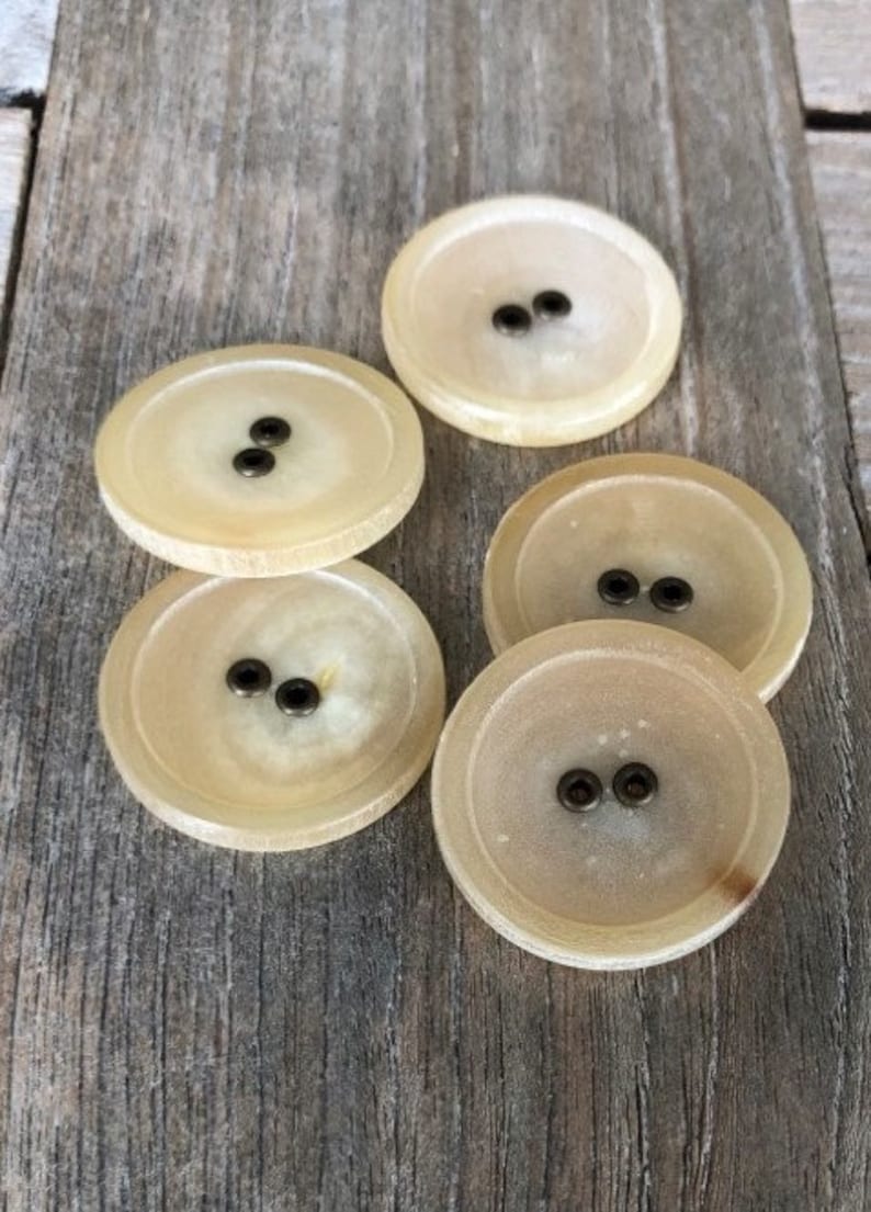 May include: Five round, cream-colored buttons with two brass buttonholes each.