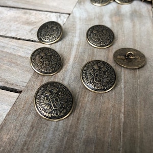 以下が含まれることがあります： 黒地に金色の文字が書かれた、金色の金属製のボタンが6個セットです。ボタンには、王冠と「BURG-CO-TYR 4780 ARCHID AUST-DUX」という文字が書かれた紋章が描かれています。