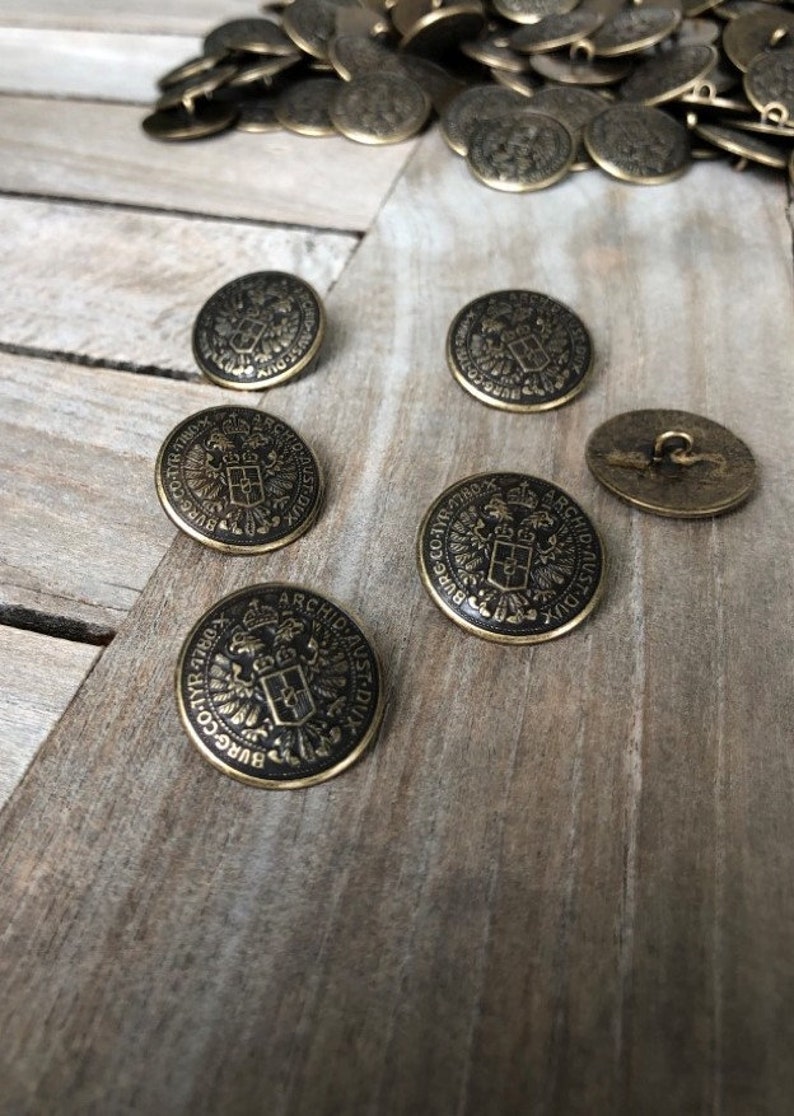 以下が含まれることがあります： 黒地に金色の文字が書かれた、金色の金属製のボタンが6個セットです。ボタンには、王冠と「BURG-CO-TYR 4780 ARCHID AUST-DUX」という文字が書かれた紋章が描かれています。