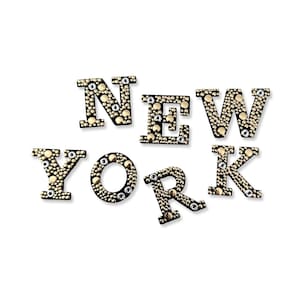 May include: Gold and silver studded letters spelling out "NEW YORK" on a white background.