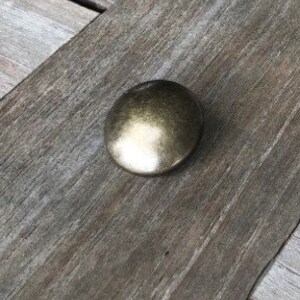 Peut inclure: Un bouton rond en m&eacute;tal de couleur or antique avec une surface lisse l&eacute;g&egrave;rement bomb&eacute;e.