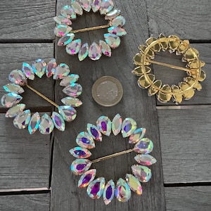 Puede incluir: Cuatro cierres de hebilla de vidrio iridiscente y tono dorado. Cada hebilla es un círculo de piedras de vidrio en forma de lágrima con una barra de metal de tono dorado en el centro.