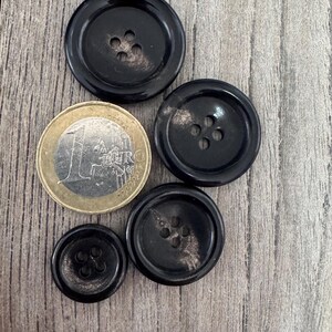K&ouml;nnte beinhalten: Vier schwarze Kn&ouml;pfe mit einer marmorierten Oberfl&auml;che und jeweils vier L&ouml;chern. Die Kn&ouml;pfe sind in einem Halbkreis mit einer Euro-M&uuml;nze in der Mitte angeordnet.