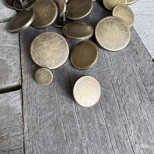 May include: A pile of antique gold-toned metal buttons with a distressed finish. The buttons are round and have a flat back.