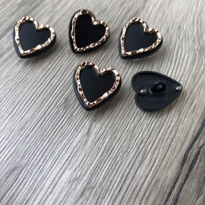 May include: Five black heart-shaped buttons with gold trim. The buttons have a raised design and a flat back.