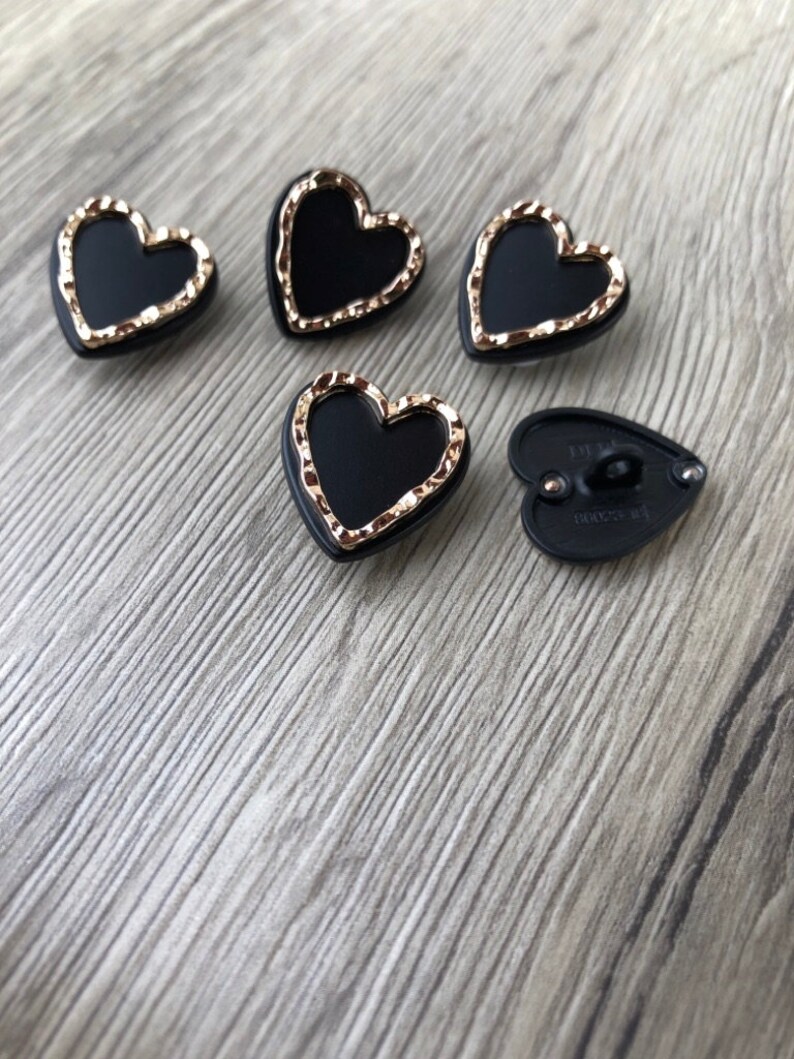 May include: Five black heart-shaped buttons with gold trim. The buttons have a raised design and a flat back.