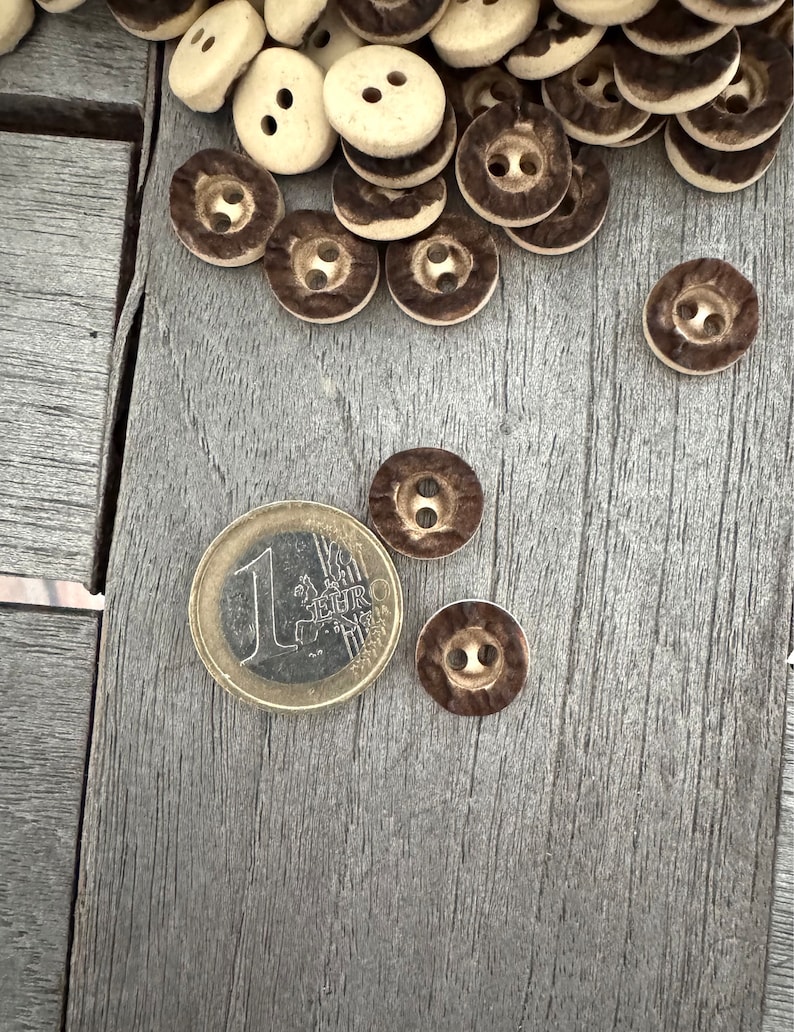 Peut inclure: Un tas de boutons bruns et blancs avec un motif brun et blanc. Il y a une pi&egrave;ce de 1 euro dans l'image.