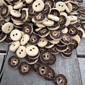 Peut inclure: Un grand tas de boutons en c&eacute;ramique brun et blanc avec deux trous chacun. Les boutons sont dispos&eacute;s de mani&egrave;re al&eacute;atoire et sont tous de la m&ecirc;me taille.
