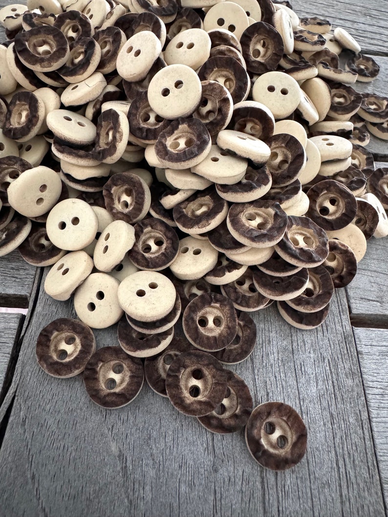 Peut inclure: Un grand tas de boutons en c&eacute;ramique brun et blanc avec deux trous chacun. Les boutons sont dispos&eacute;s de mani&egrave;re al&eacute;atoire et sont tous de la m&ecirc;me taille.