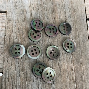 May include: Nine iridescent mother-of-pearl buttons with four holes each. The buttons are arranged in a cluster on a wooden surface.