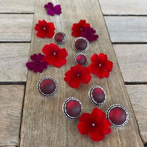 May include: Assortment of red and silver earrings with a floral design. The earrings feature a round, silver setting with a red, cabochon-shaped stone.