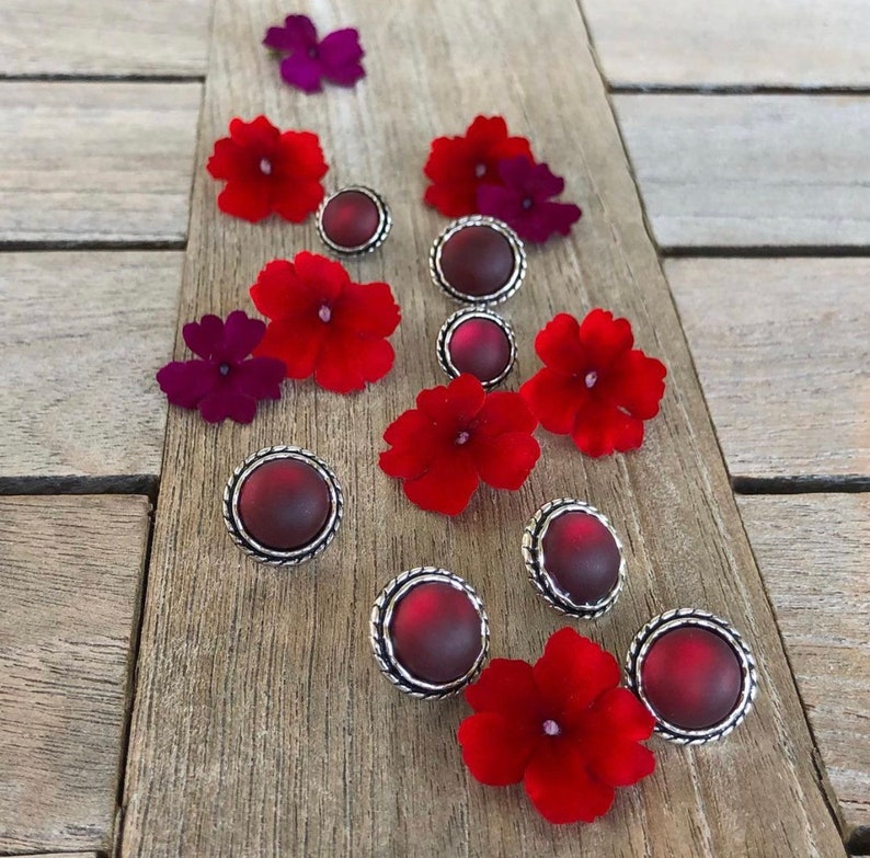 May include: Assortment of red and silver earrings with a floral design. The earrings feature a round, silver setting with a red, cabochon-shaped stone.