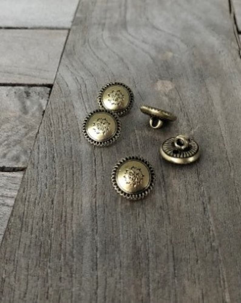 May include: Four gold-toned buttons with a decorative floral design. The buttons have a raised edge and a flat back.