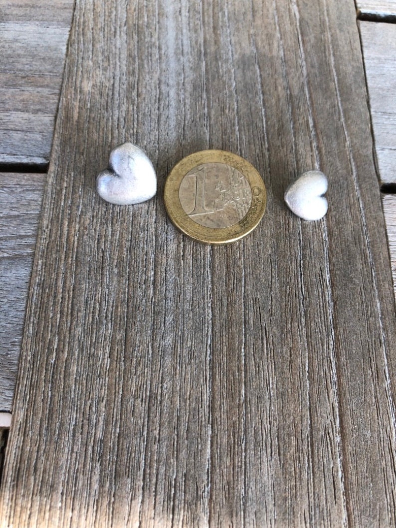 May include: Two small silver heart-shaped charms, one on each side of a silver euro coin.