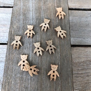Peut inclure: Dix boutons en bois en forme d'ours, chacun avec deux trous. Les boutons sont de couleur brun clair et ont un design simple.
