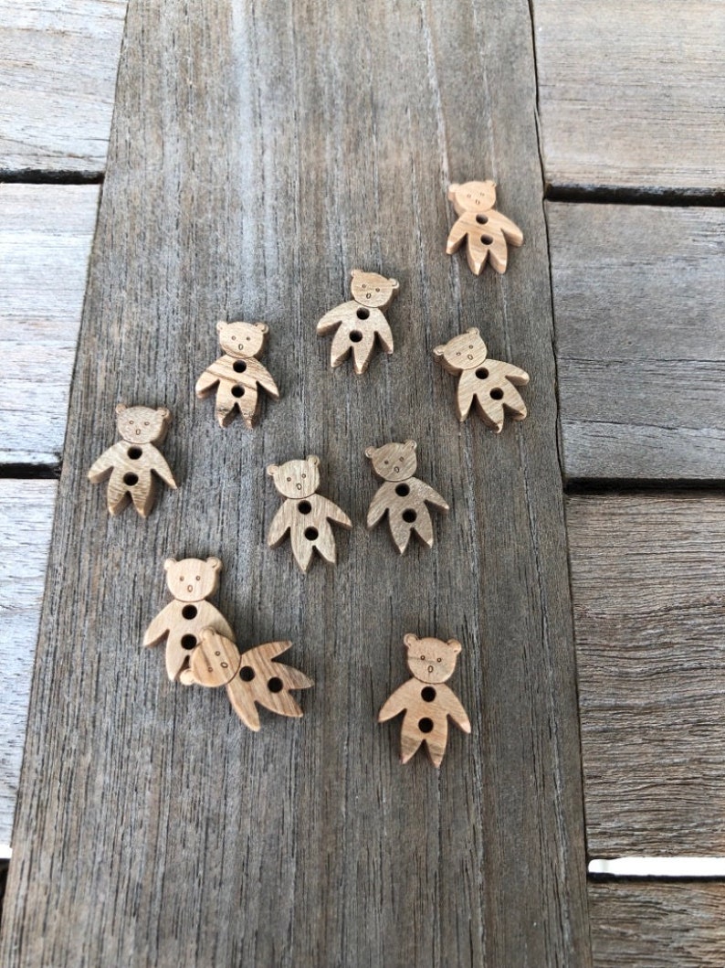 Peut inclure: Dix boutons en bois en forme d'ours, chacun avec deux trous. Les boutons sont de couleur brun clair et ont un design simple.