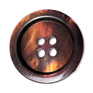 May include: A large, round button with a lustrous, iridescent finish. The button features a dark brown outer rim and a central area with a blend of brown, orange, and gold tones. Four evenly spaced holes are visible in the center.