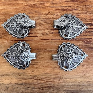 May include: Four silver heart-shaped metal clasps with intricate floral designs. Each clasp has a hook on the side.