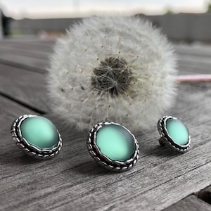 May include: Three silver and green round buttons with a textured edge. The buttons have a smooth, slightly translucent green centre.