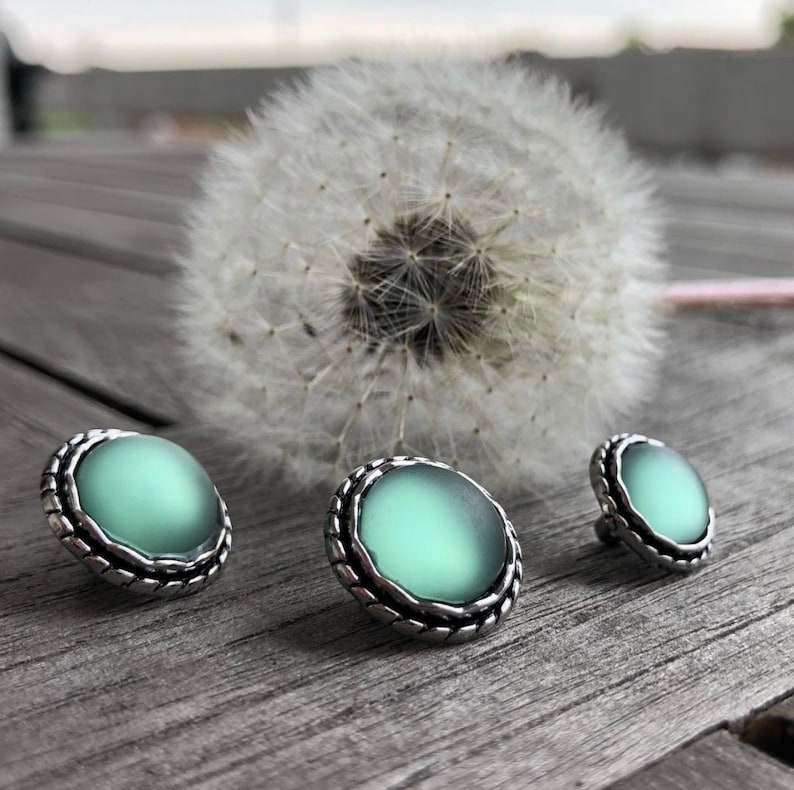May include: Three silver and green round buttons with a textured edge. The buttons have a smooth, slightly translucent green centre.