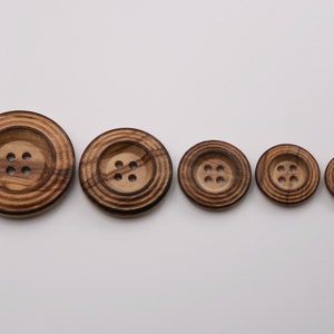 May include: Five wooden buttons in different sizes, all with four holes and a concentric ring pattern. The buttons are brown with darker brown stripes.