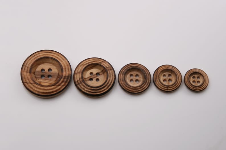 May include: Five wooden buttons in different sizes, all with four holes and a concentric ring pattern. The buttons are brown with darker brown stripes.