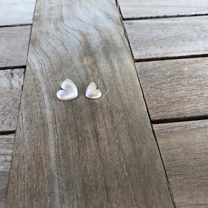 May include: Two silver heart-shaped charms on a wooden surface.