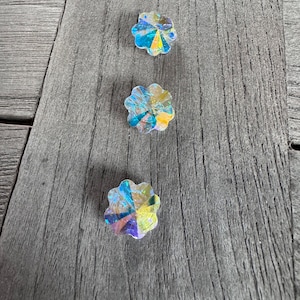 Op de afbeelding: Drie regenboogkleurige kristallen bloemvormige versieringen op een houten oppervlak.