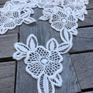 Op de afbeelding: Witte kant met een bloemenpatroon. De kant is delicaat en ingewikkeld, met kleine bloemen en bladeren.