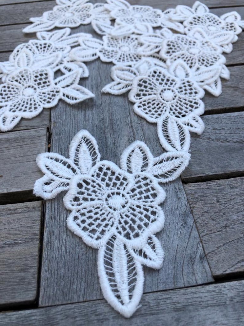 Op de afbeelding: Witte kant met een bloemenpatroon. De kant is delicaat en ingewikkeld, met kleine bloemen en bladeren.