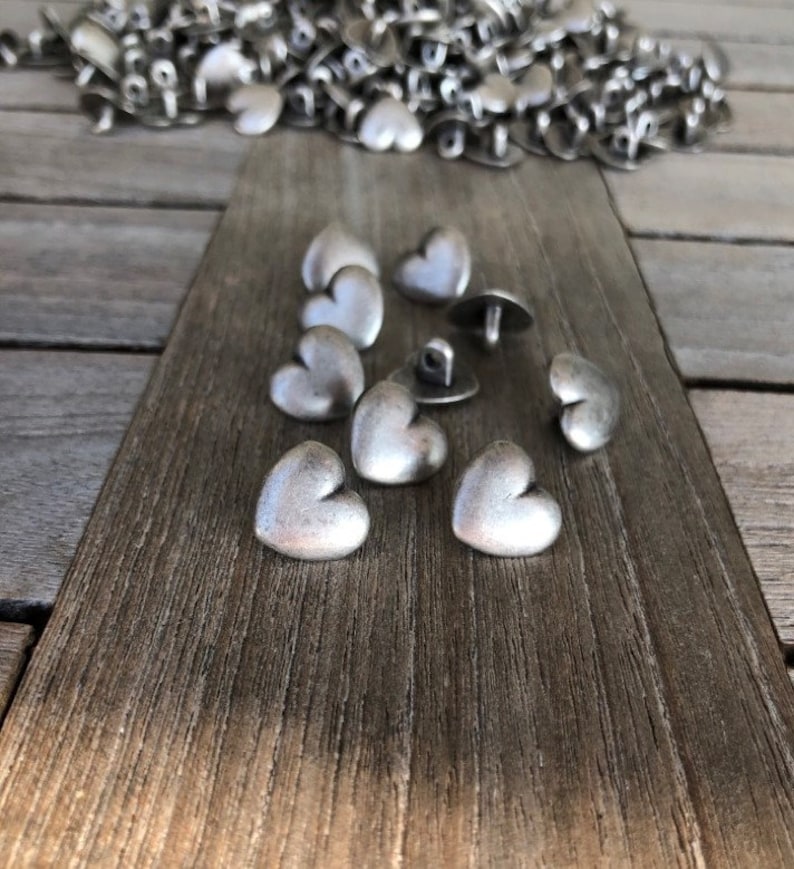 May include: A group of silver heart-shaped buttons with a shiny finish. The buttons are arranged on a wooden surface.