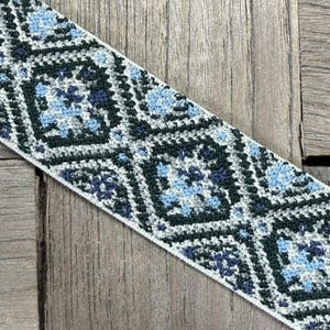 Könnte beinhalten: Nahaufnahme einer dekorativen Borte mit geometrischem Muster. Die Borte weist ein sich wiederholendes Design aus Quadraten in Blau-, Grün- und Weißtönen auf. Die Borte ist diagonal auf einer Holzoberfläche platziert.
