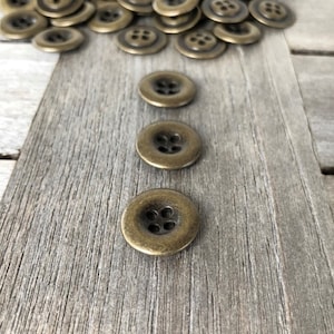 Peut inclure: Un groupe de boutons en métal doré antique à quatre trous chacun. Les boutons sont éparpillés sur une surface en bois. Trois boutons sont alignés en rangée sur le bois.