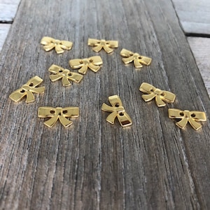 May include: Ten gold-colored metal bow-shaped buttons. The buttons have two holes each.